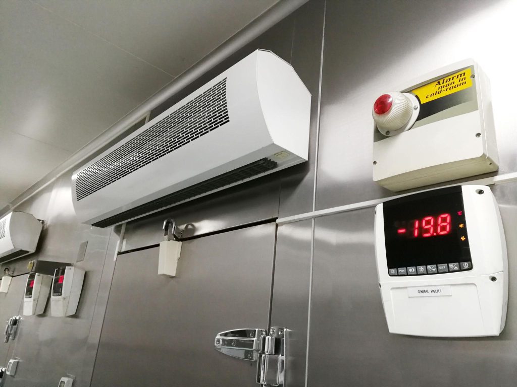 Freezer room interior with wall-mounted evaporator, digital temperature controller displaying -19.8°C, and insulated freezer doors